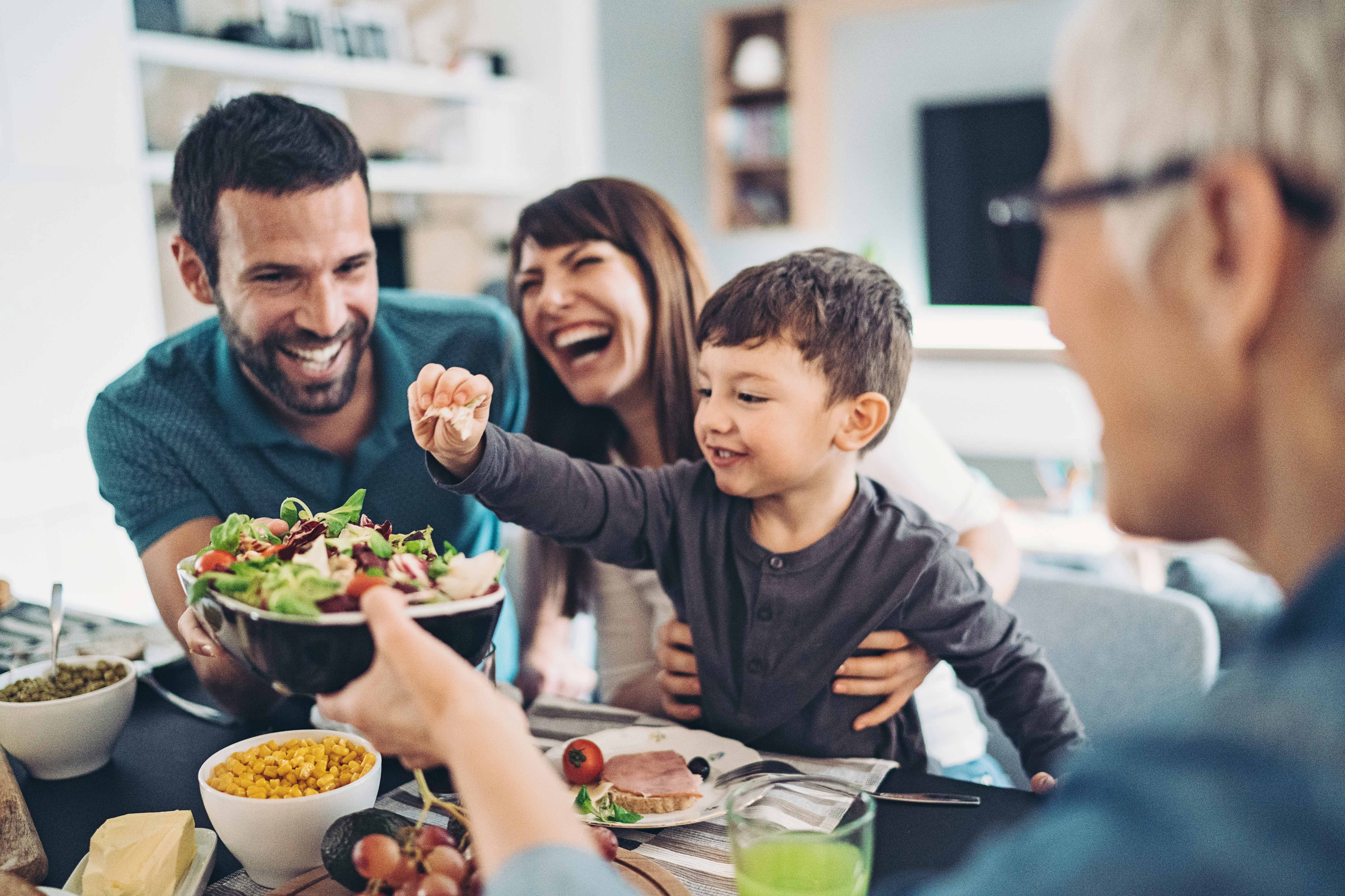 Man, woman, and child laughing over a bowl of food with a grandmother looking on