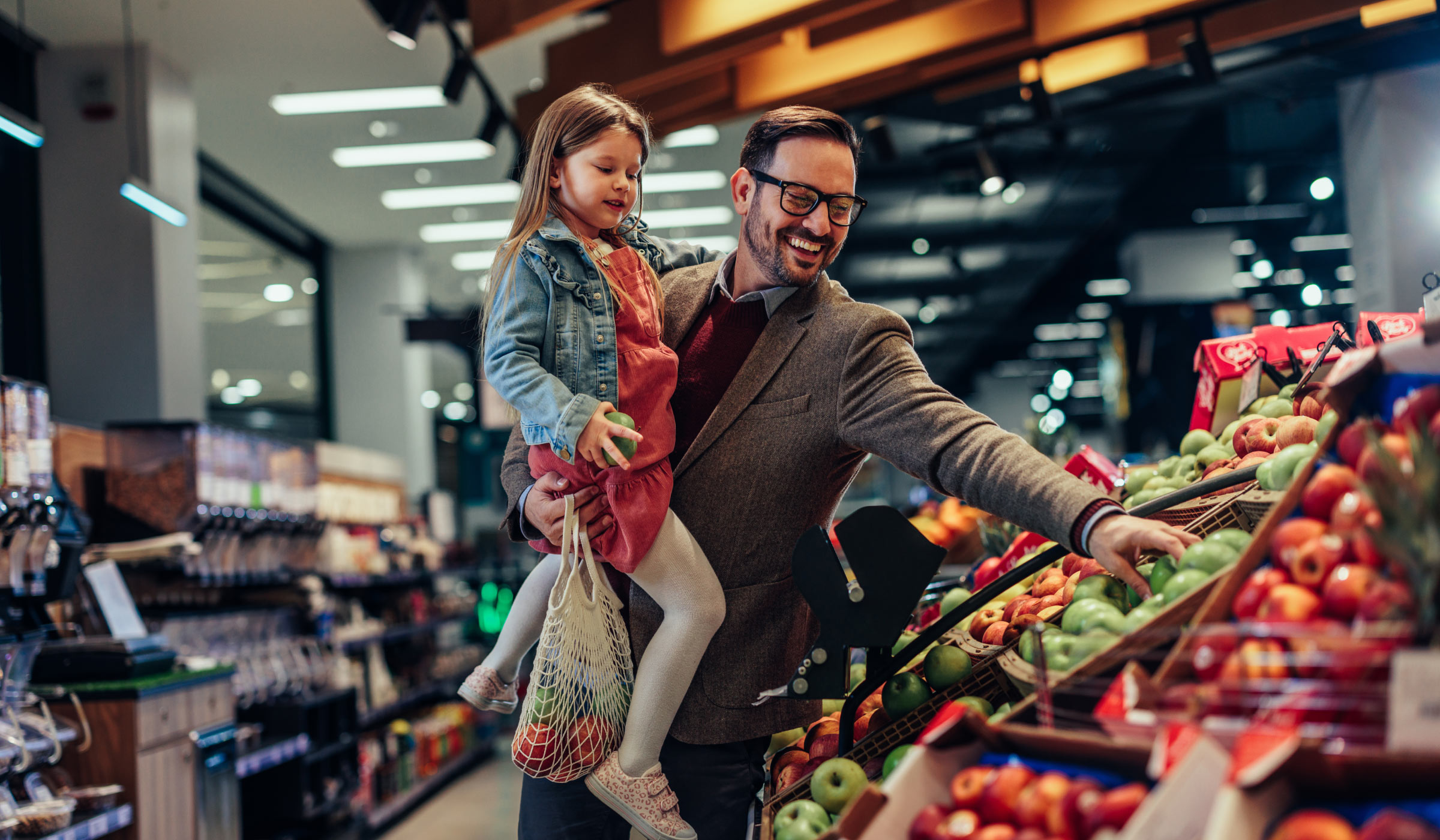 A man holding his daughter while shopping for produce in a grocery store