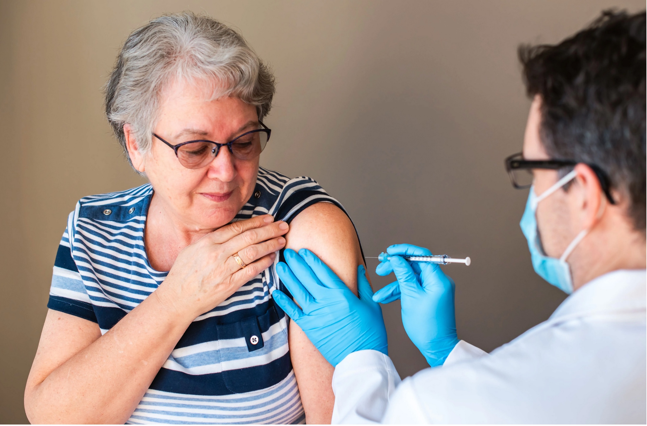 Masked medical worker giving a vaccination to an elderly woman.